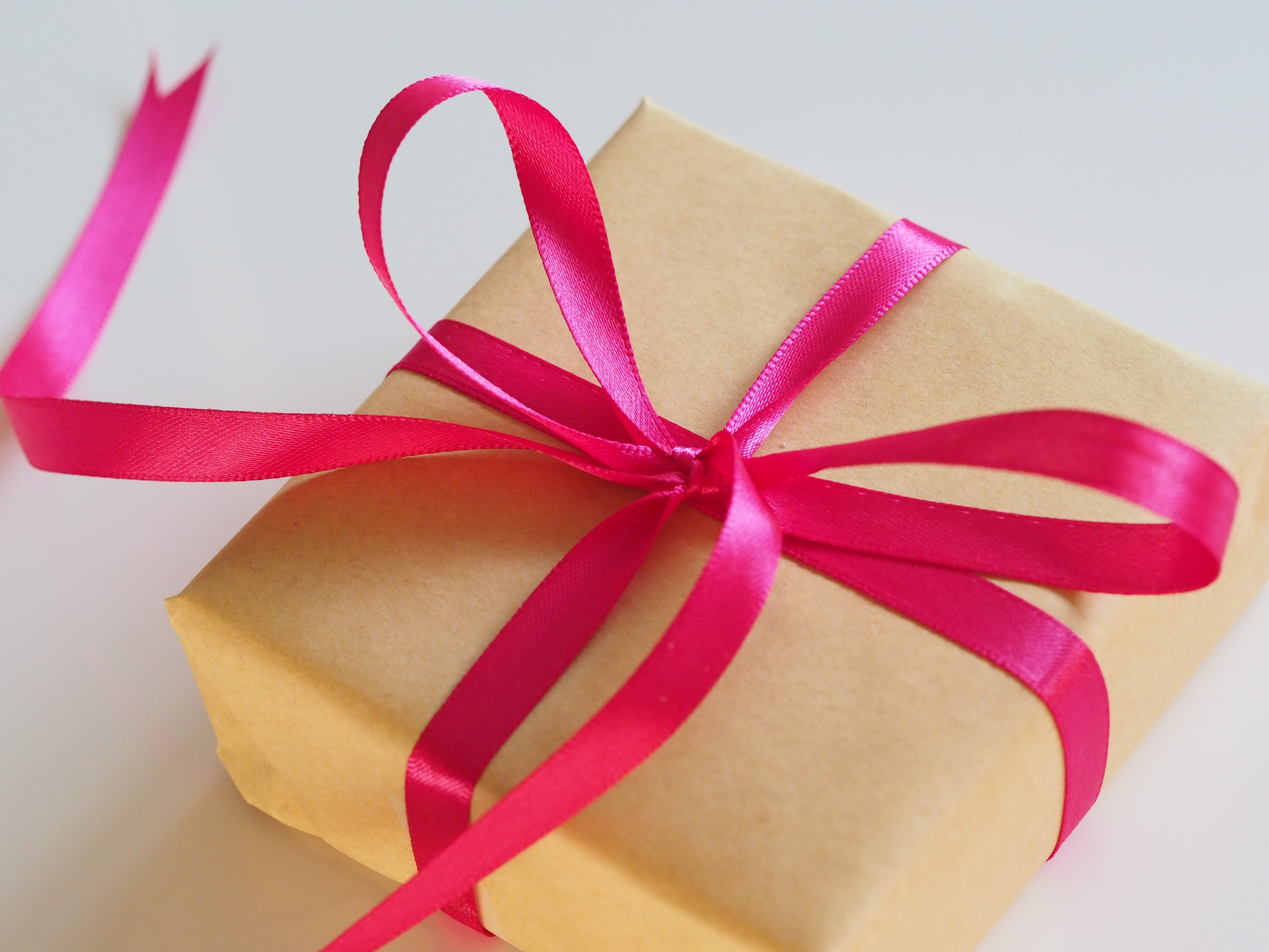 A flat box gift in brown wrapping paper with a pink ribbon tied around it. 