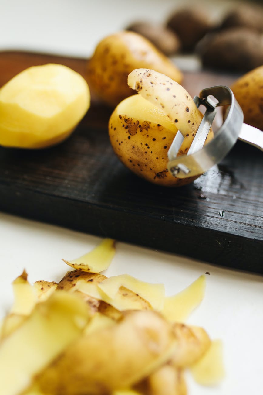 a cutting board with a potato peeler, some potatoes and some potato peels 