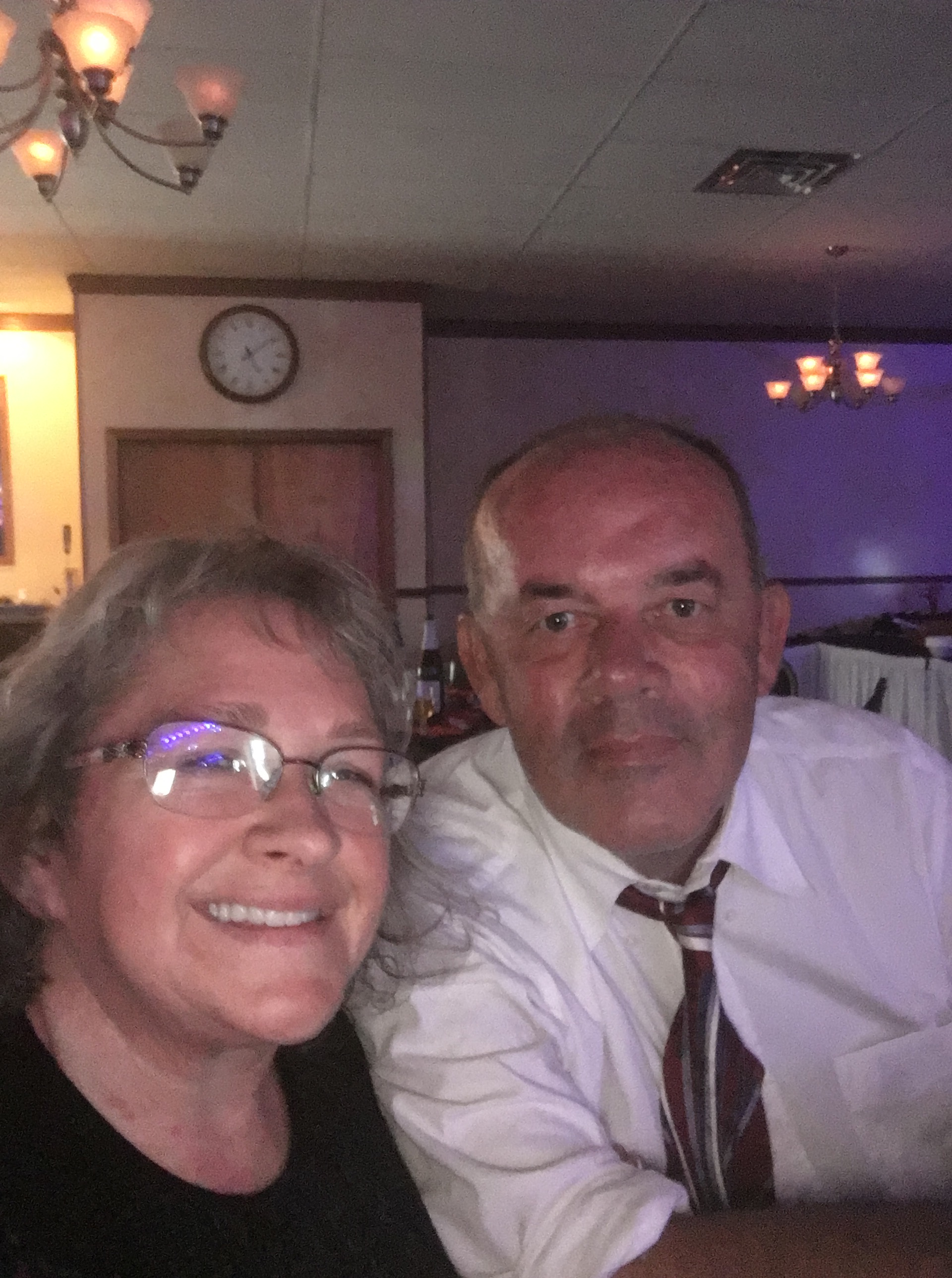 Amy and Ken dressed up. Ken wearing a button dress shirt and tie, and Amy a dress. They are seated at a table. 