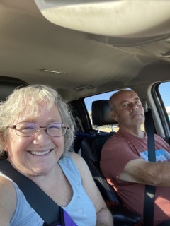 Ken driving wearing a t-shirt, and Amy in a tank top in passenger seat. Both smiling. 